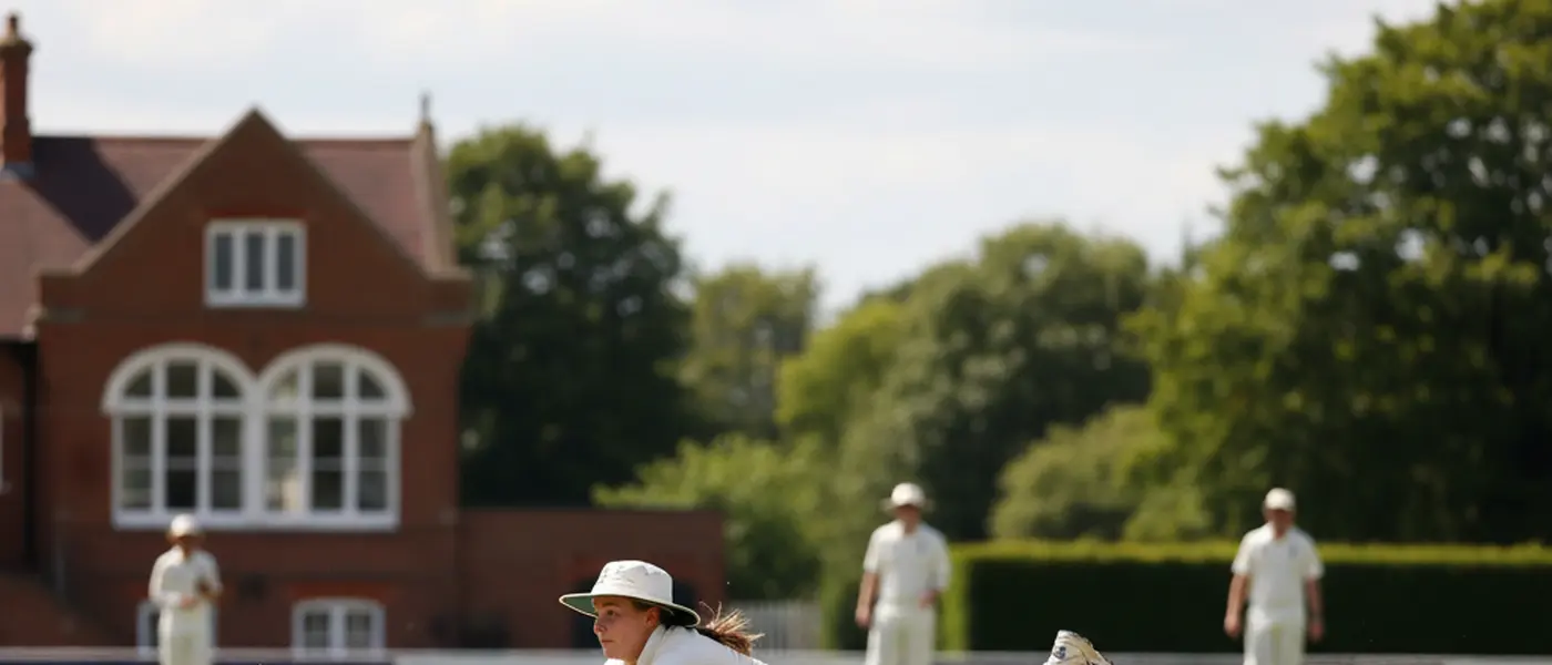 Female cricket player diving to field the ball on a grass pitch