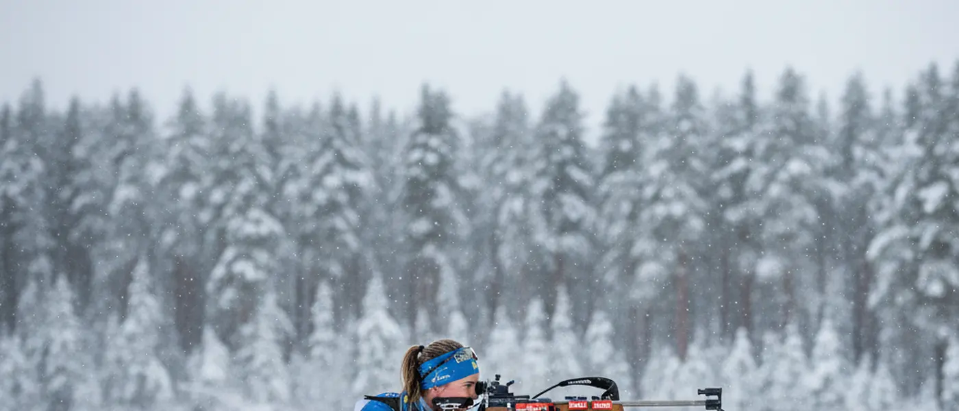 Biatlet i liggande skjutposition på en snötäckt skjutbana i en vintrig skog
